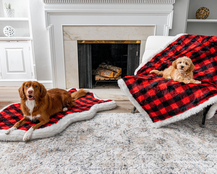 dogs resting on buffalo plaid dog bed and blanket set in front of fireplace